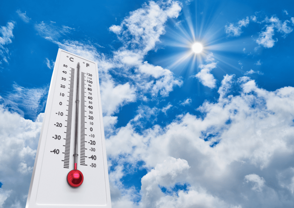 A thermometer showing high temperatures against a bright blue sky with scattered clouds and a shining sun in the background.