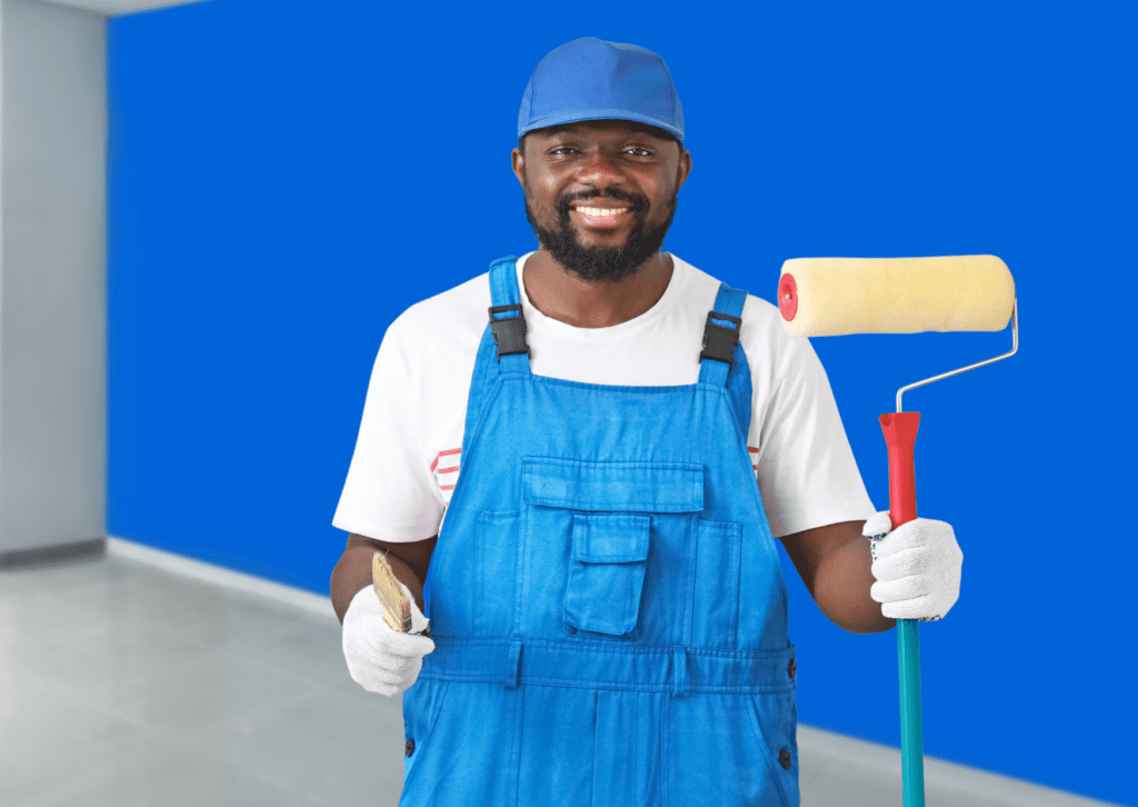 A commercial painting services painter in a uniform, holding a paint roller in front of a freshly painted blue wall.