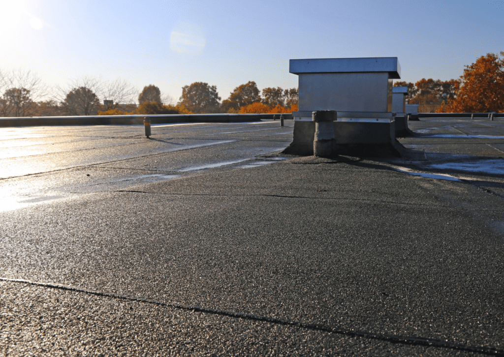 Flat rooftop with ventilation units and autumn trees in the background, illuminated by morning sunlight under a clear sky.