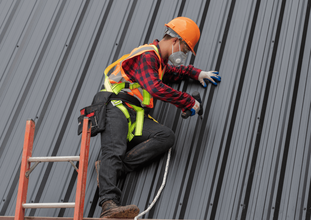 A worker in safety gear and a hard hat installs metal roofing sheets, demonstrating the use of durable roof materials.