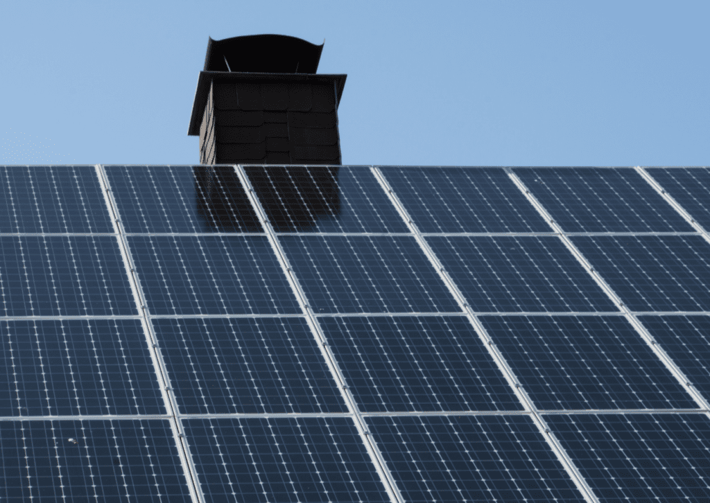 Close-up of solar panels installed on a rooftop with a chimney in the background, under a clear blue sky.