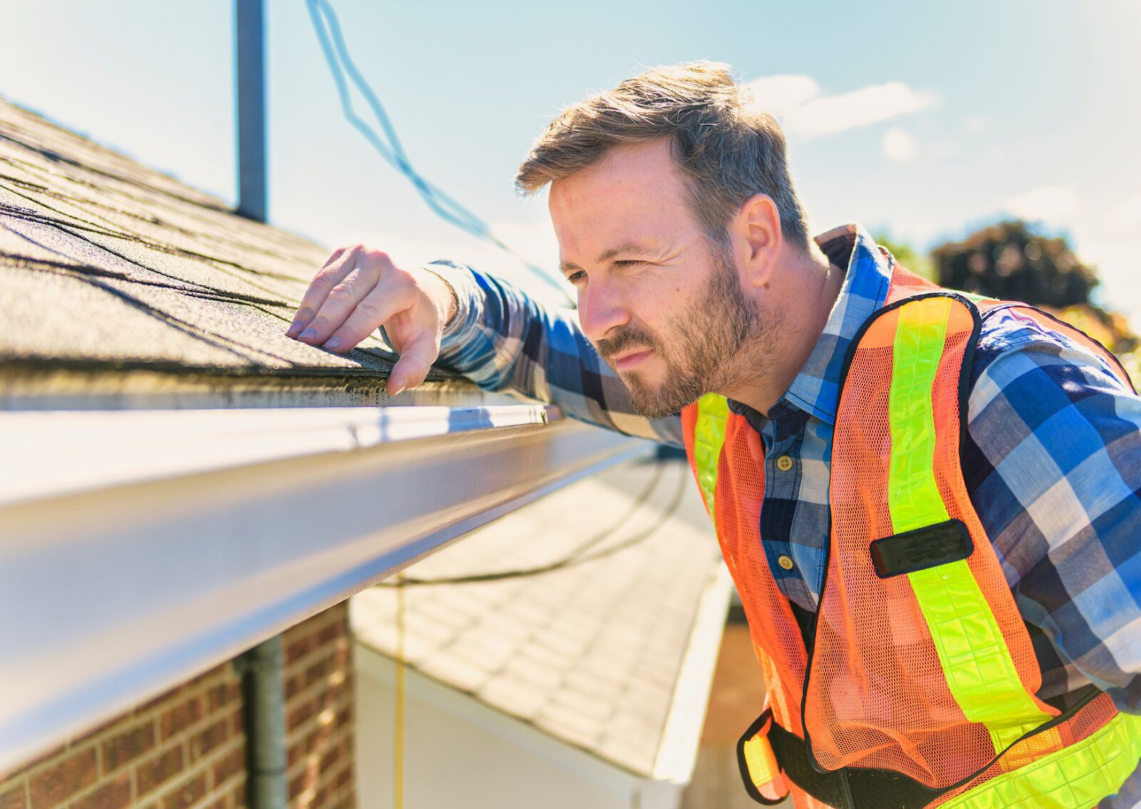 Inspector examining shingles and gutter, demonstrating a roof inspection process for home safety and maintenance.