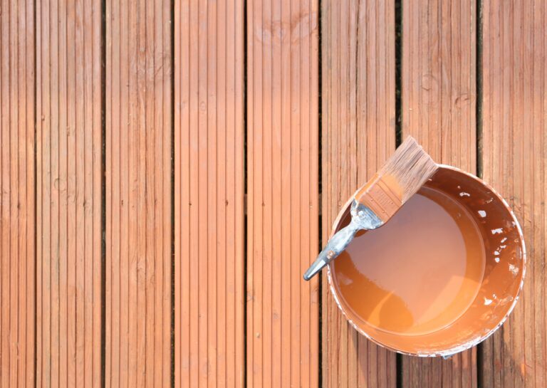 Close-up of a deck being painted, with a paintbrush and a bucket of paint, illustrating how to paint a deck effectively.