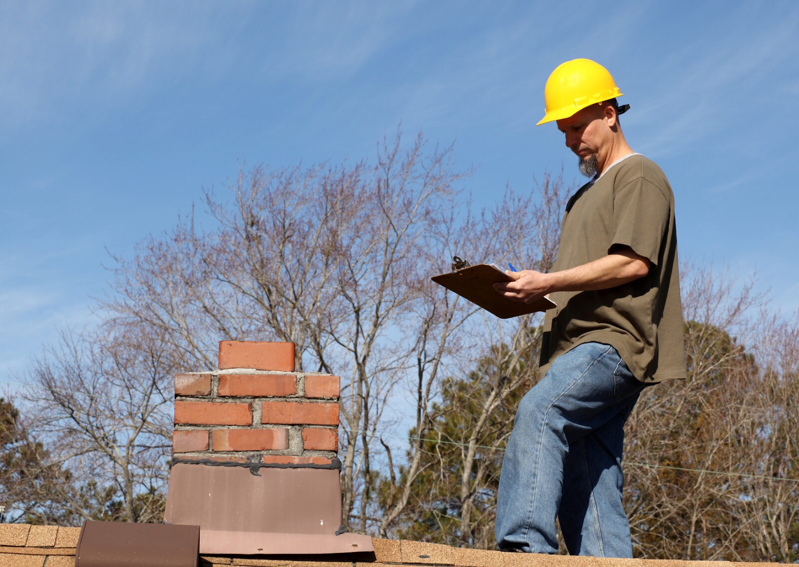 An inspector with a clipboard on the roof near the chimney performs a roof inspection to ensure integrity and safety.