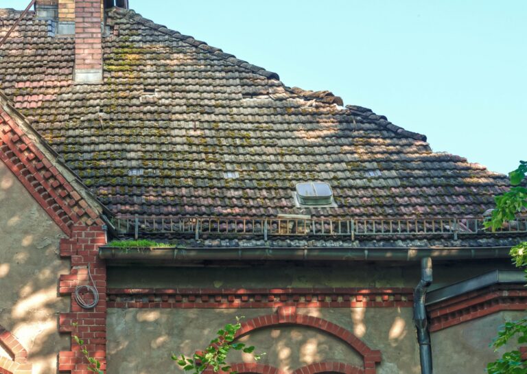 An old, weathered, and moss-covered tiled roof, with signs of deterioration that needs a new roof.