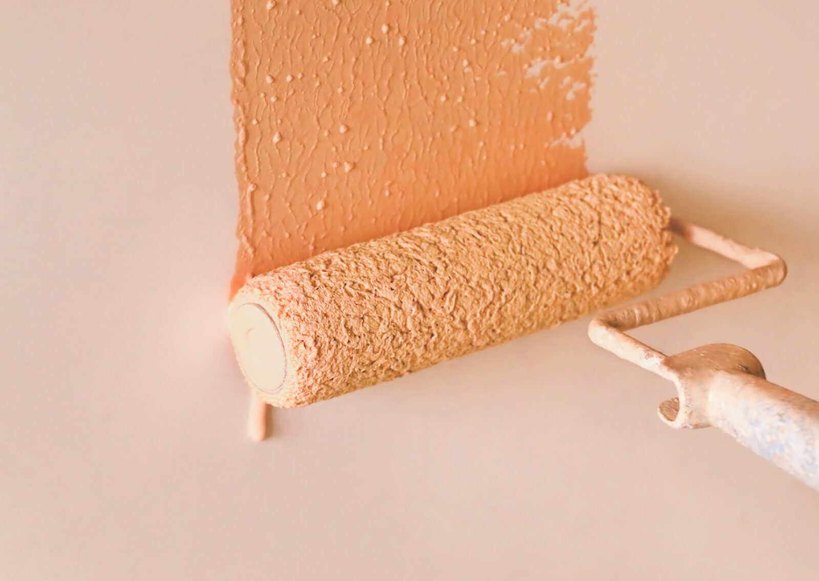 A paint roller applying textured peach-colored paint on a white wall showcases a smooth and even painting process.