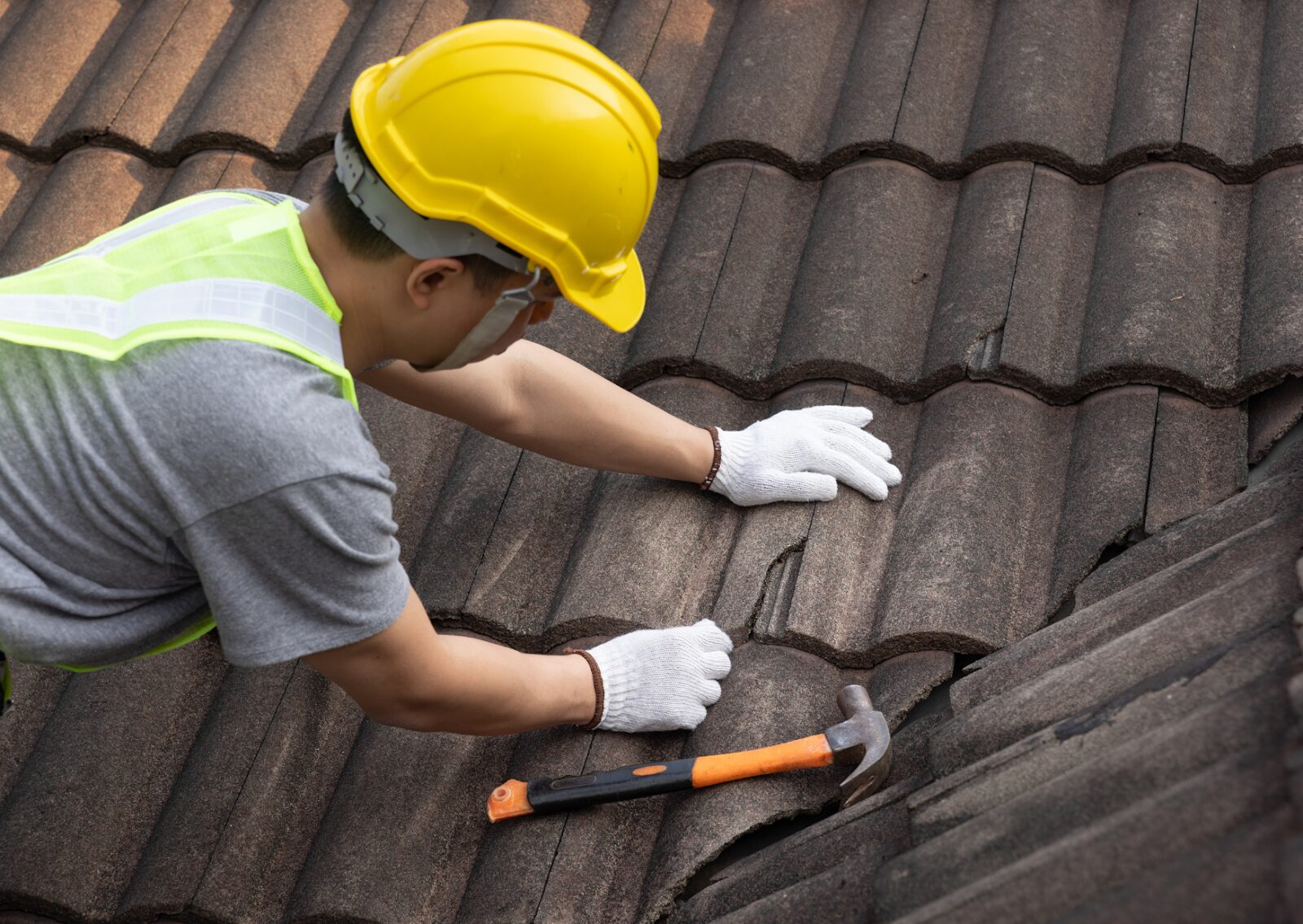 A worker from a local roofing company repairing a tiled roof, demonstrating the detail and professional roofing services.