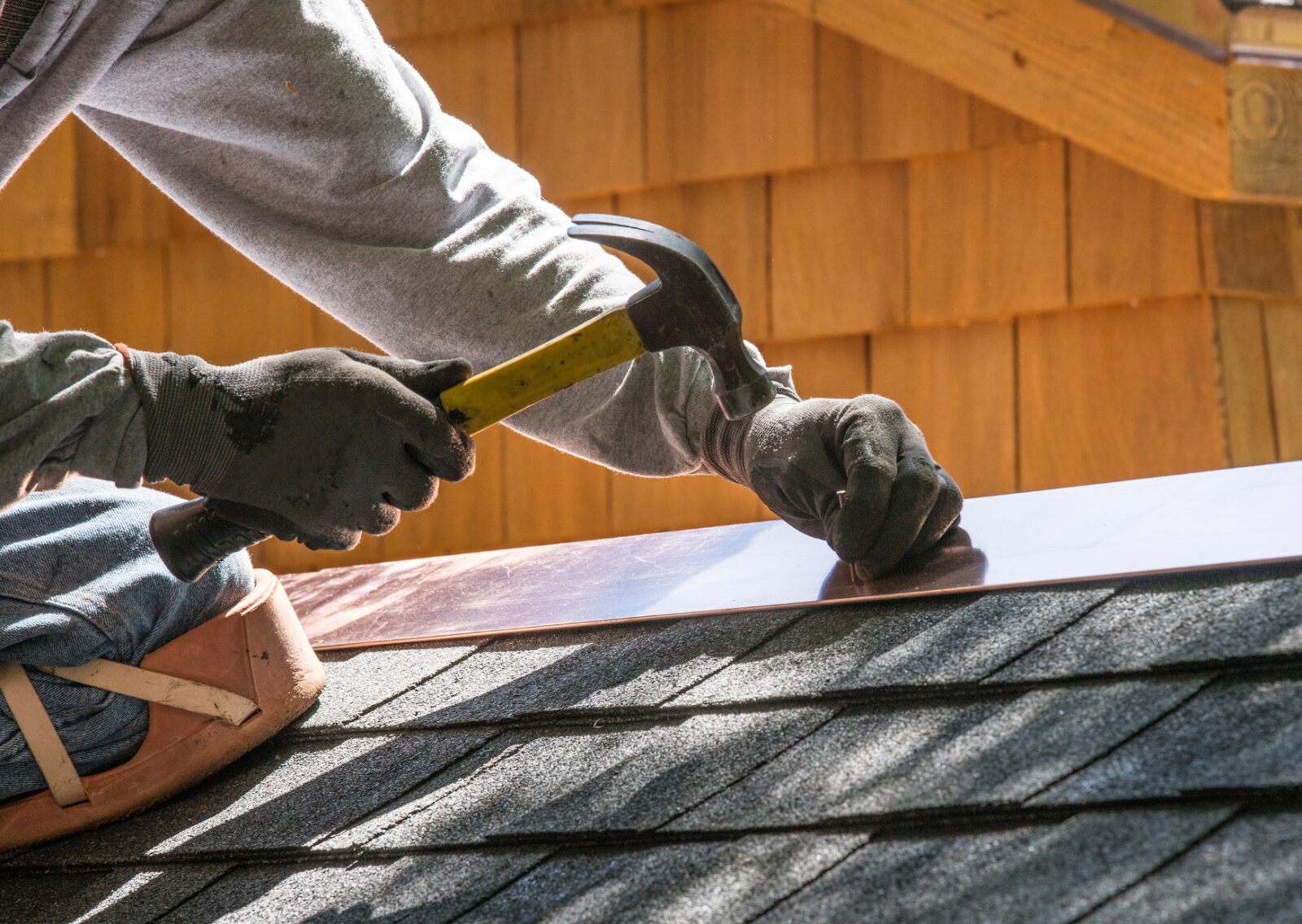 A worker's hands with gloves using a hammer to fix shingles during a roof repair, highlighting detailed craftsmanship.