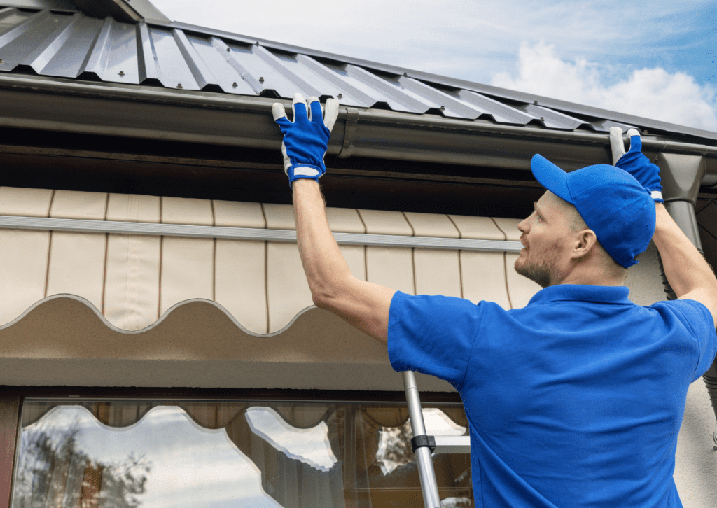 Worker in blue uniform installing or inspecting a gutter system on a metal roof, ensuring proper drainage and protection.