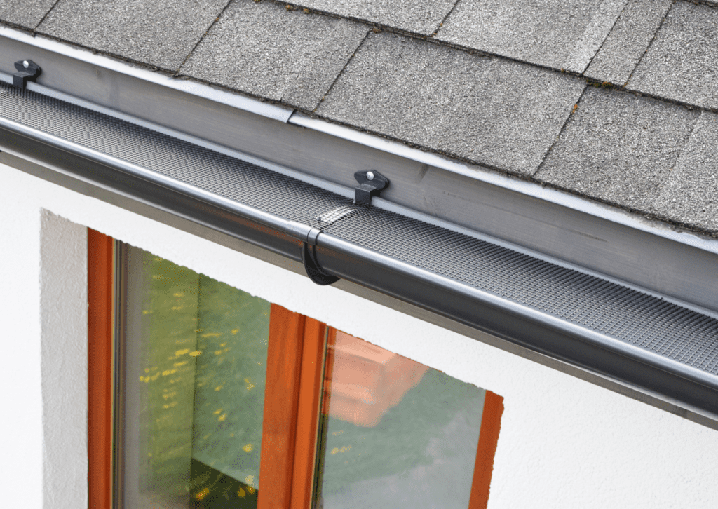 Close-up of a black gutter with a guard installed on a shingled roof, providing effective water drainage and protection.