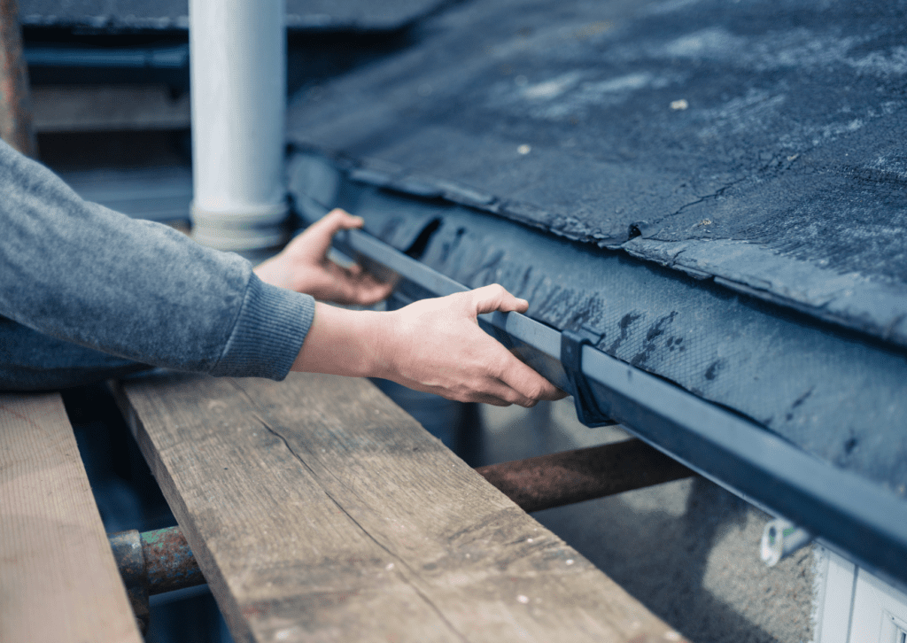 Hands installing a new gutter on a roof, representing quality gutter replacement services for home maintenance.