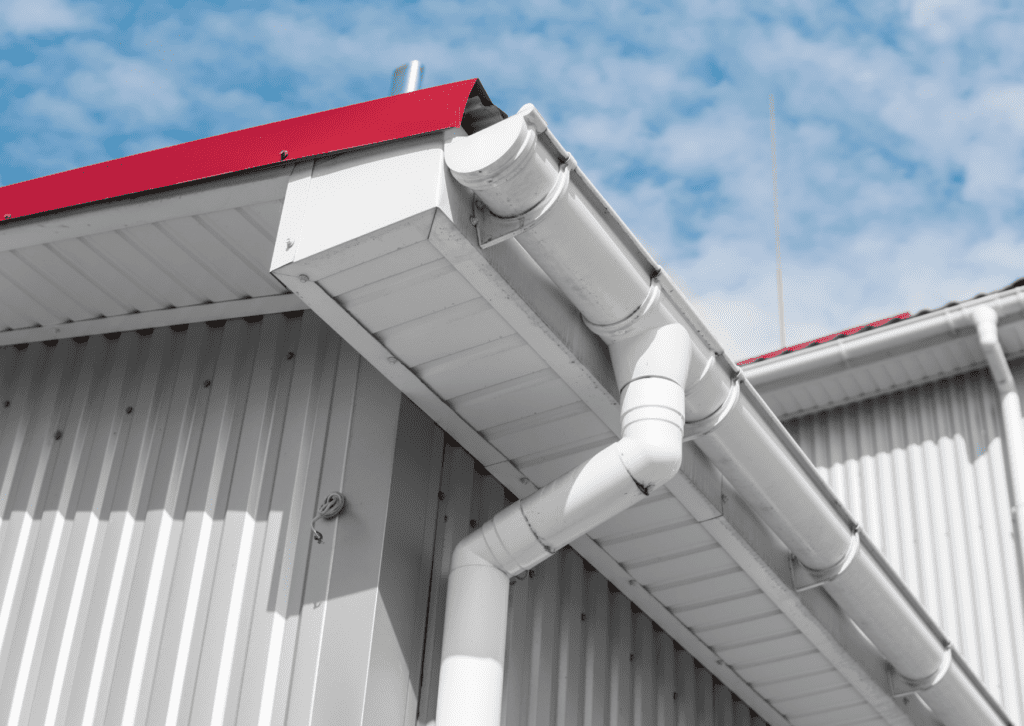 A white gutter system is installed on a metal roof under a clear sky, highlighting the durable roof and gutter solutions.