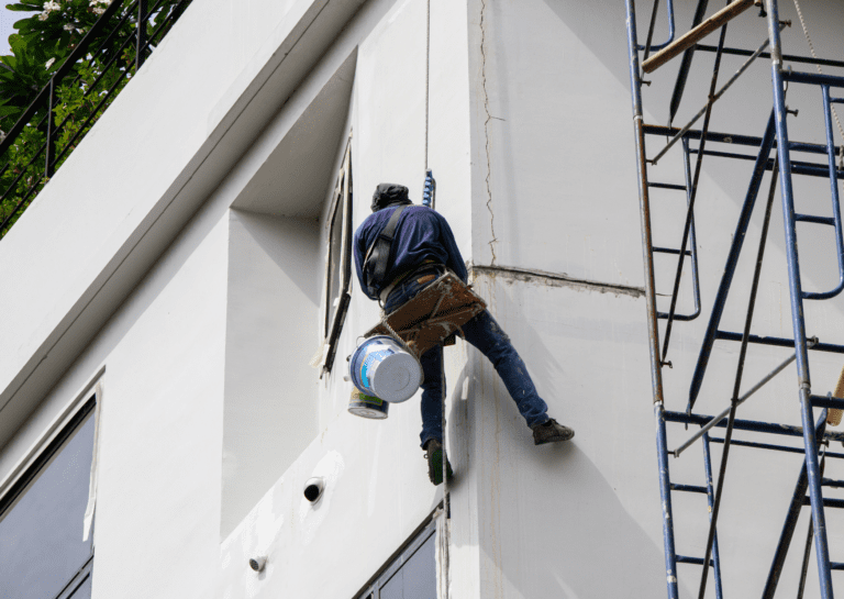 Painter working on a building facade, considering the effects of paint and temperature on the final finish.