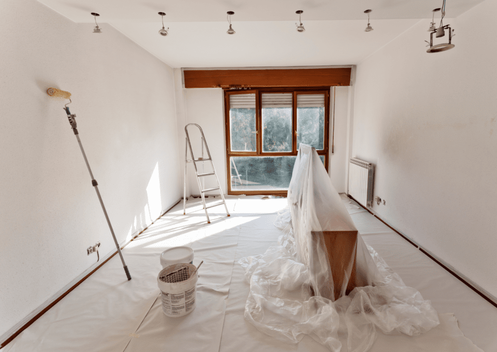 An empty room prepared for painting with furniture covered, a ladder, and paint supplies ready to refresh the walls.