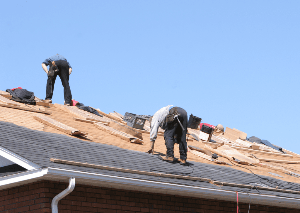 Roofers replacing shingles under a clear sky, highlighting a residential roofing project in progress.