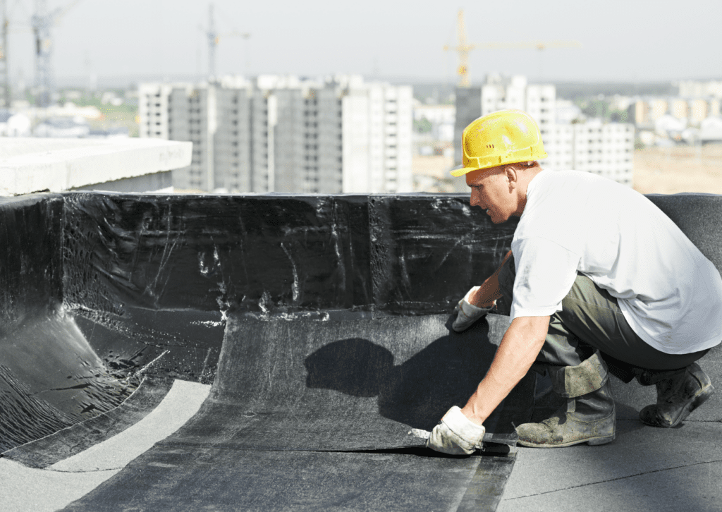 Roofer applying waterproofing membrane on a flat roof of a commercial building, ensuring long-lasting protection.