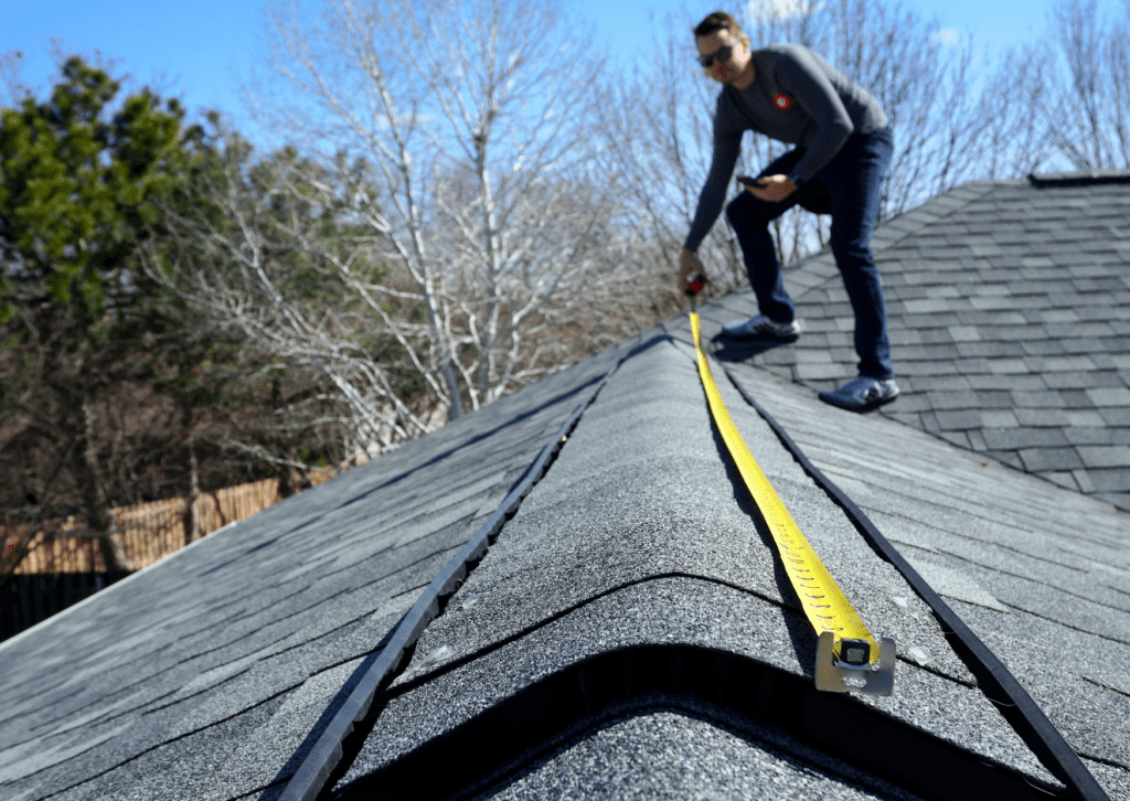 Contractor measuring roof length with a tape measure for an estimate.