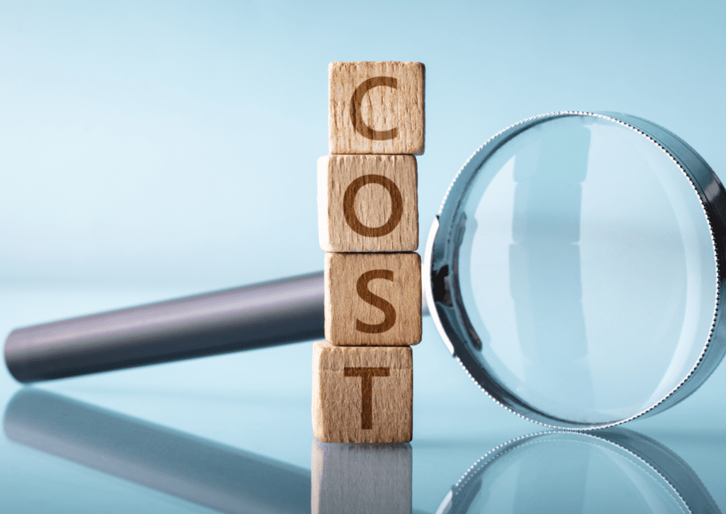 Wooden blocks spelling 'COST' with a magnifying glass symbolizing cost analysis or estimation.