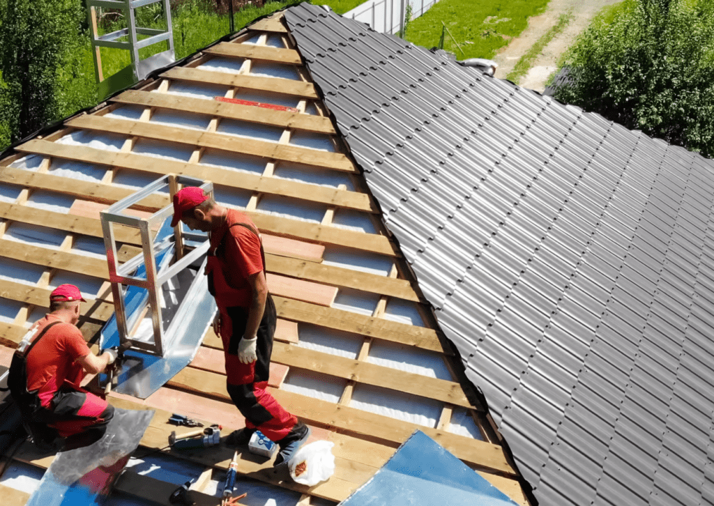 Roofers install metal roofing panels and insulation for a durable roof solution.