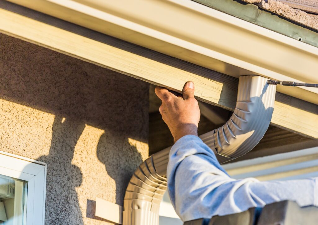 Worker installing a rain gutter and downspout for proper water drainage.