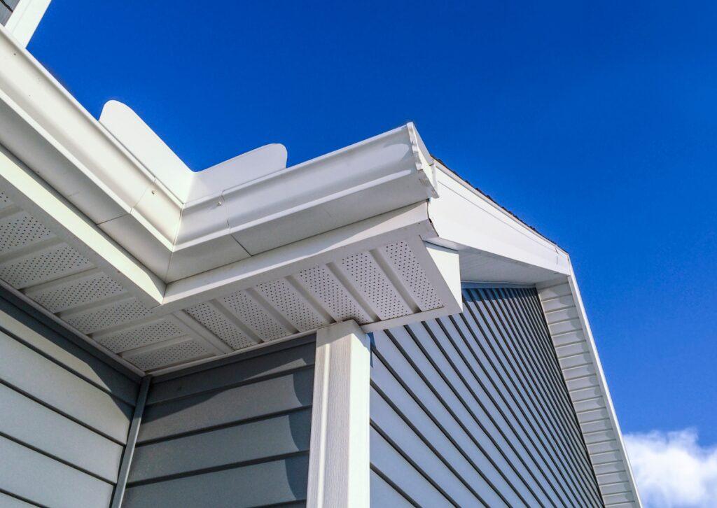 The white gutter system on a house with blue siding under a clear sky.