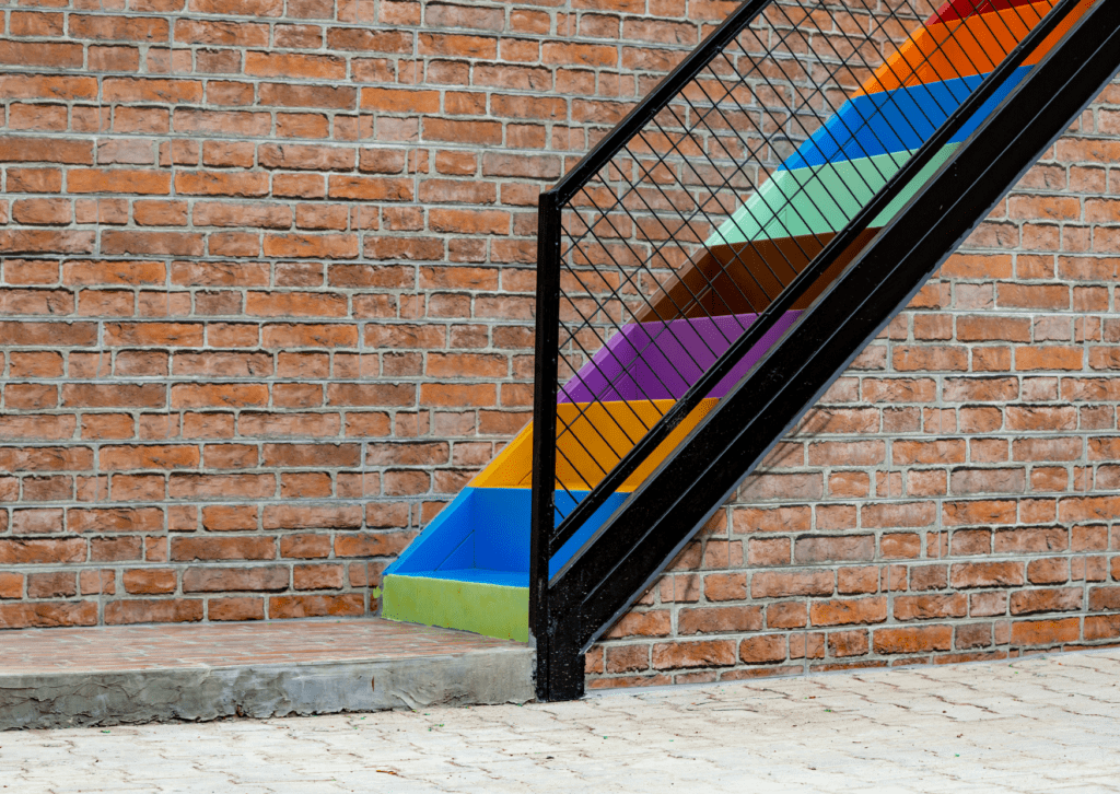 Colorful painted metal stairs against a brick wall, showcasing creative use of paint for stairs in an outdoor design project.