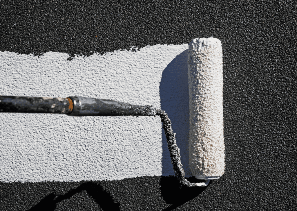 Paint roller applying white paint over a textured black surface, showcasing a smooth coverage and even application technique.