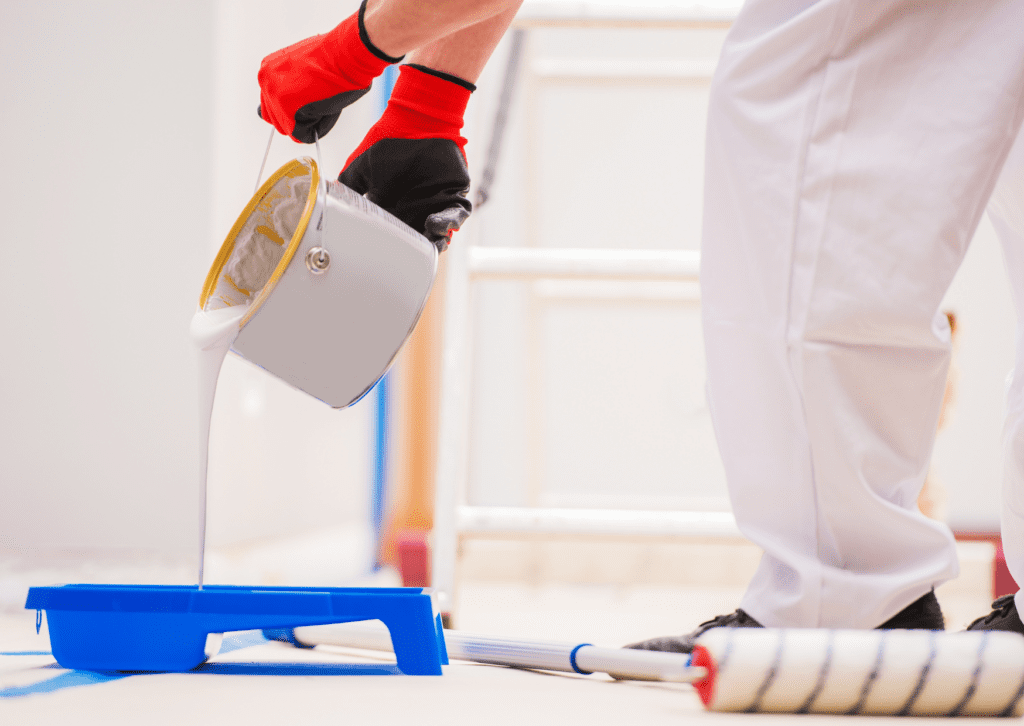 The painter pours white paint into a tray and prepares for a painting job with a roller.