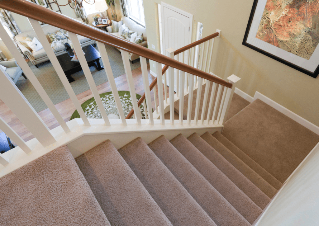 Carpeted stairs with white railing and wooden handrail, overlooking a cosy living room.