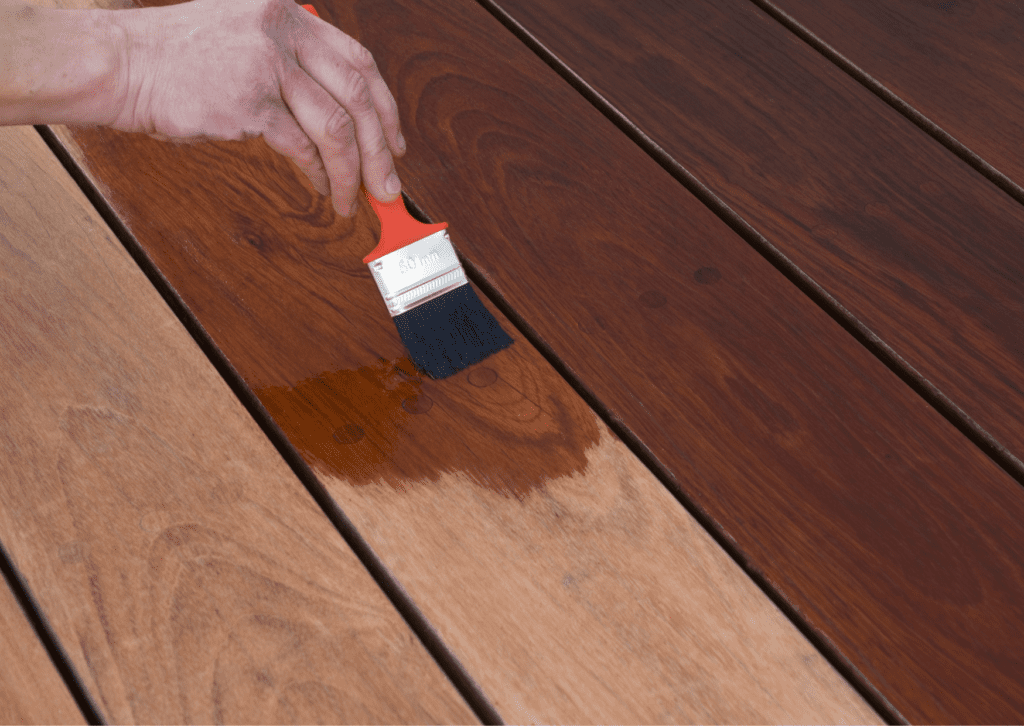 Applying stain to wooden planks with a brush, showcasing the transformation of natural wood during a wood painting project.