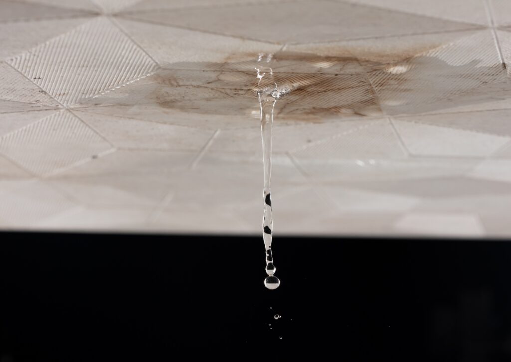 Water dripping from a stained ceiling due to damage, highlighting the need for urgent roof leak repair.