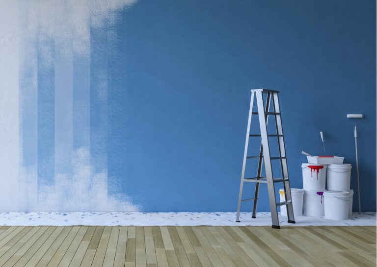 A partially painted blue wall with a ladder, paint buckets, and rollers, showcasing the interior painting process.