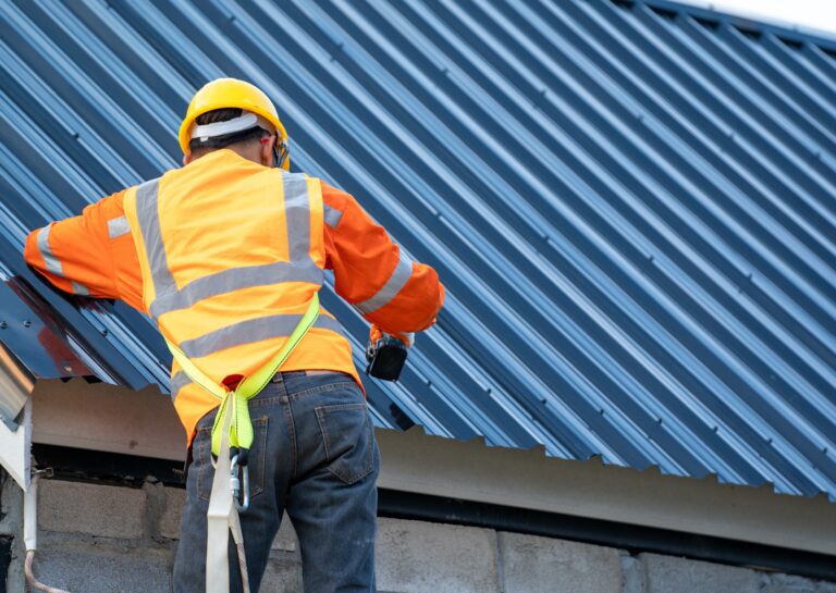 Worker in safety gear performing roofing repair and maintenance on a metal roof, using a drill for secure installation.