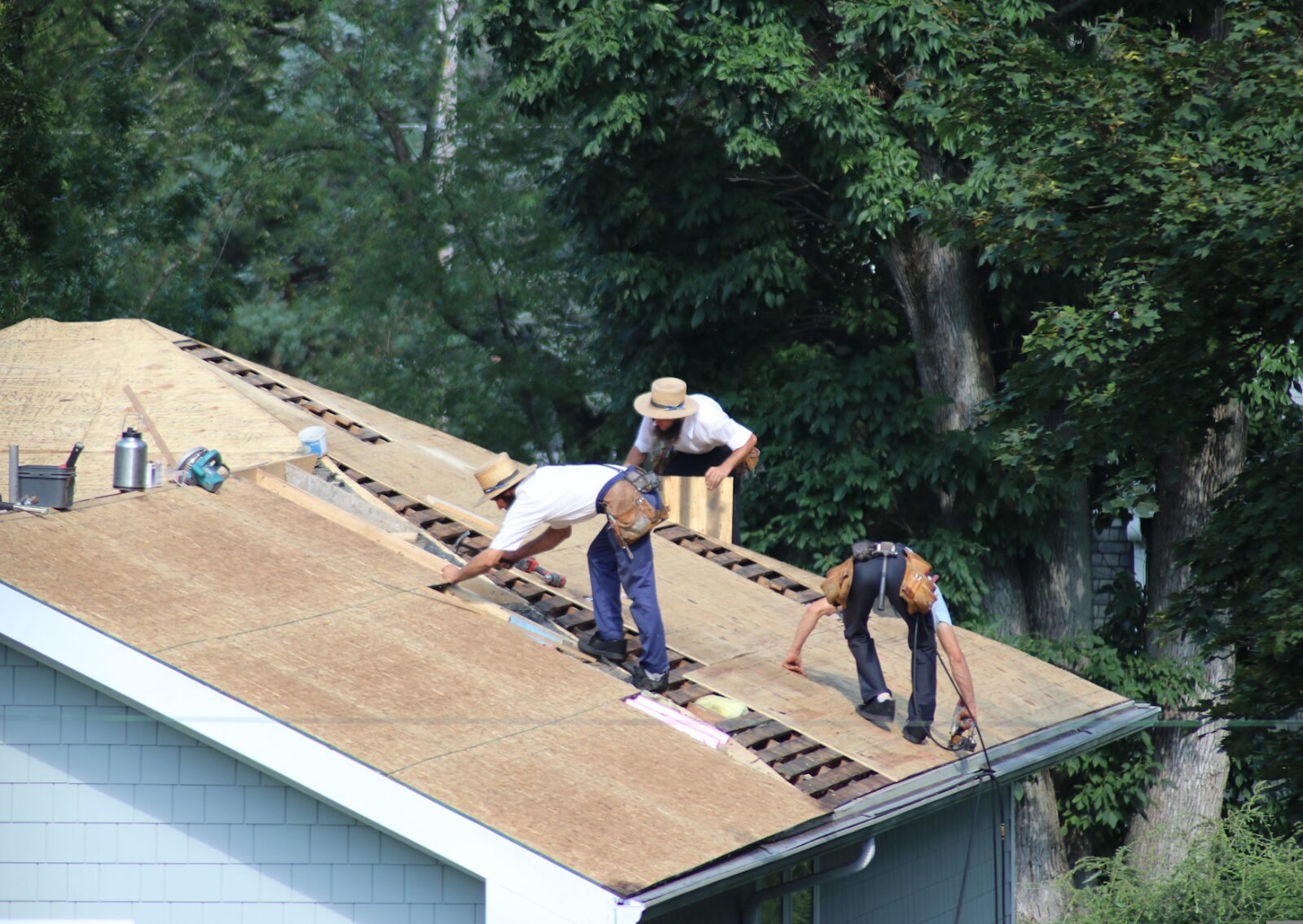 Three workers performing a residential roof replacement, removing old shingles and preparing the wooden decking.