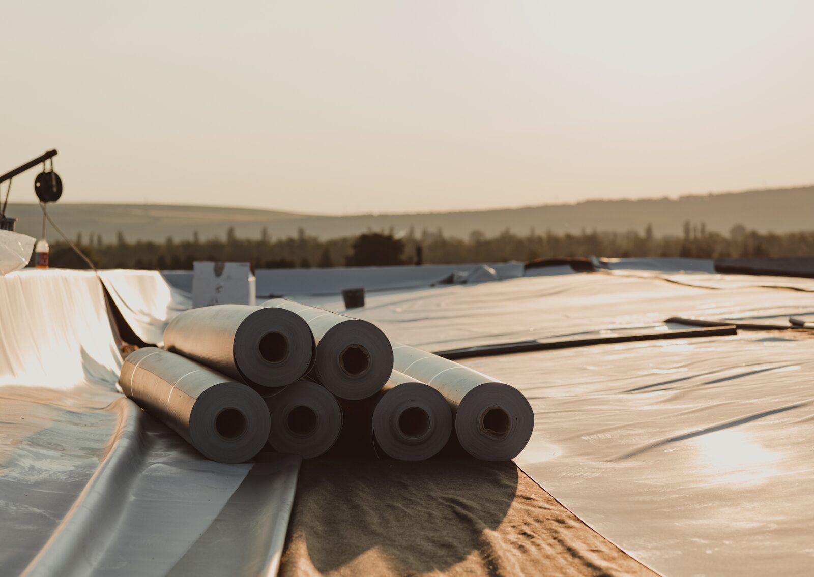 Rolls of roofing membrane material on a flat surface during a commercial roofing installation at sunset.