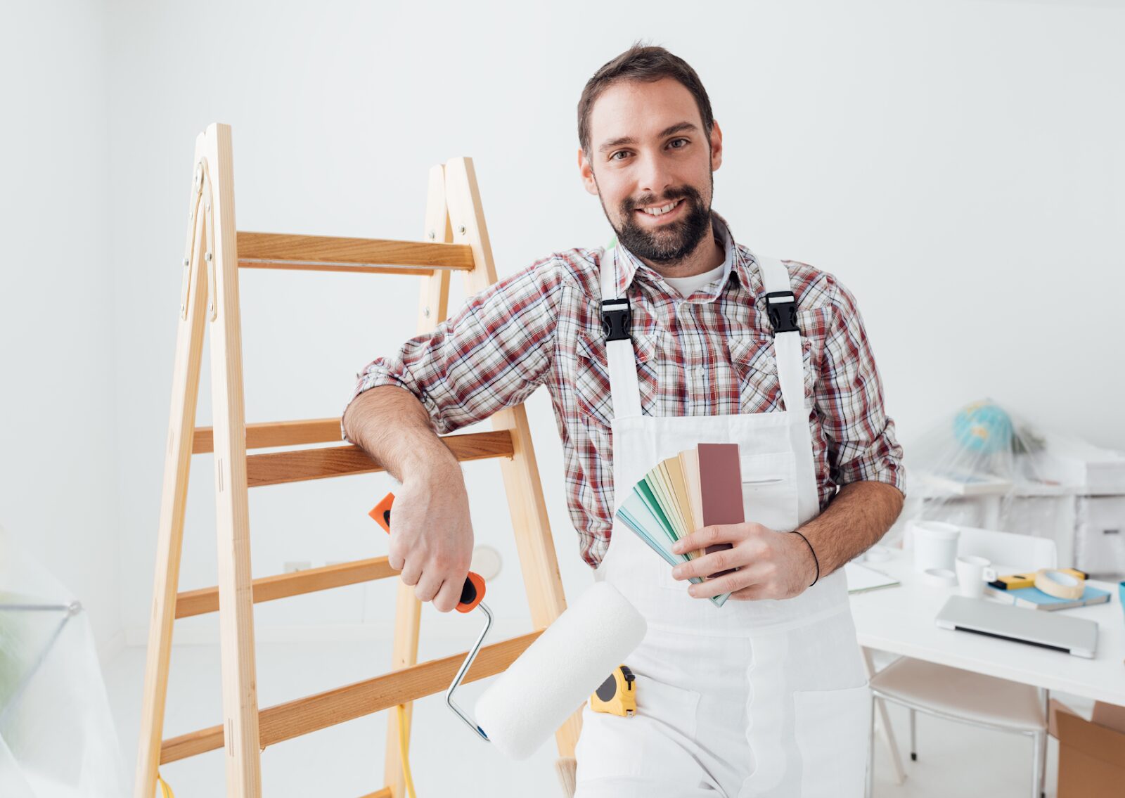 Smiling painter holding color swatches and a paint roller while standing next to a wooden ladder.
