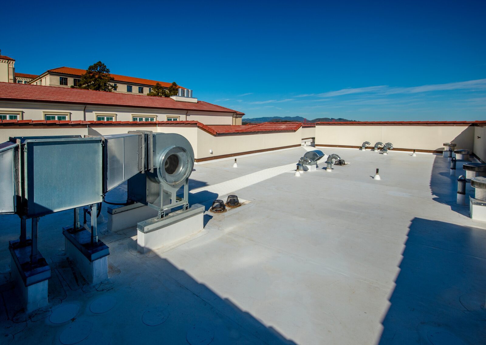 Flat white surface of a commercial roofing system with HVAC units and vents under a clear blue sky.