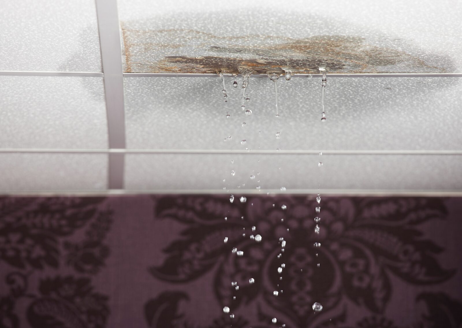 Water is leaking from a damaged ceiling with visible stains and drops falling into the room below.