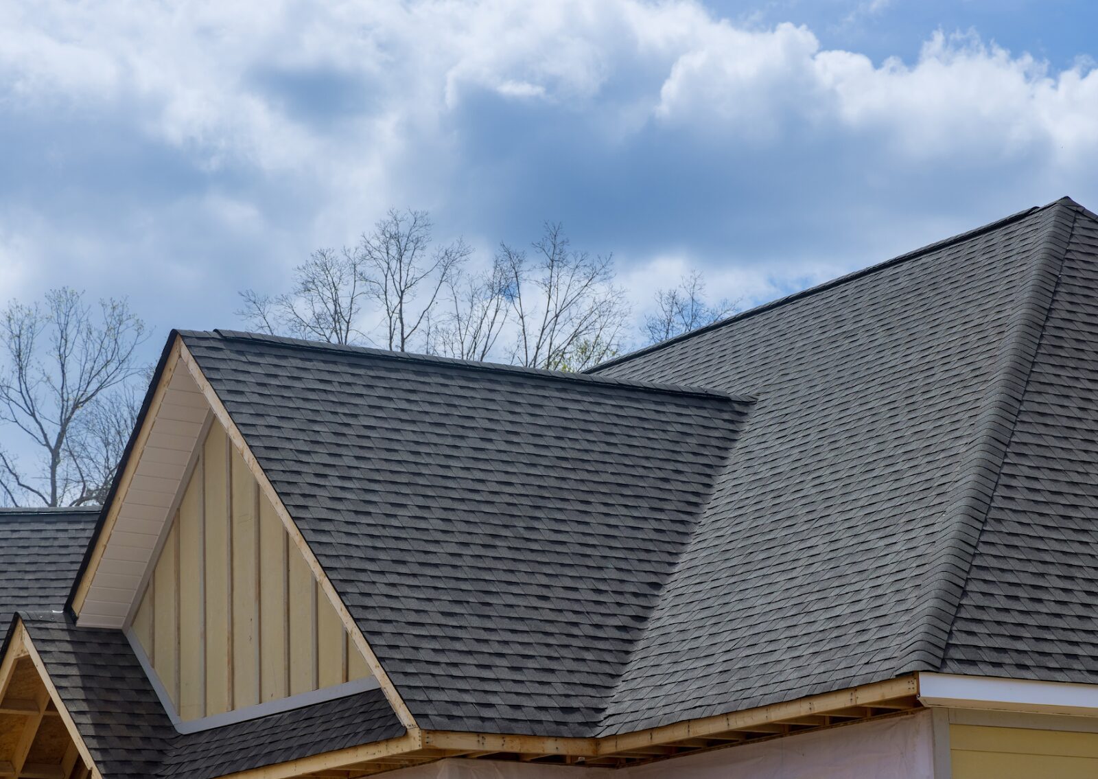 New asphalt shingle installation after roof repair for homes under a blue sky with light clouds.