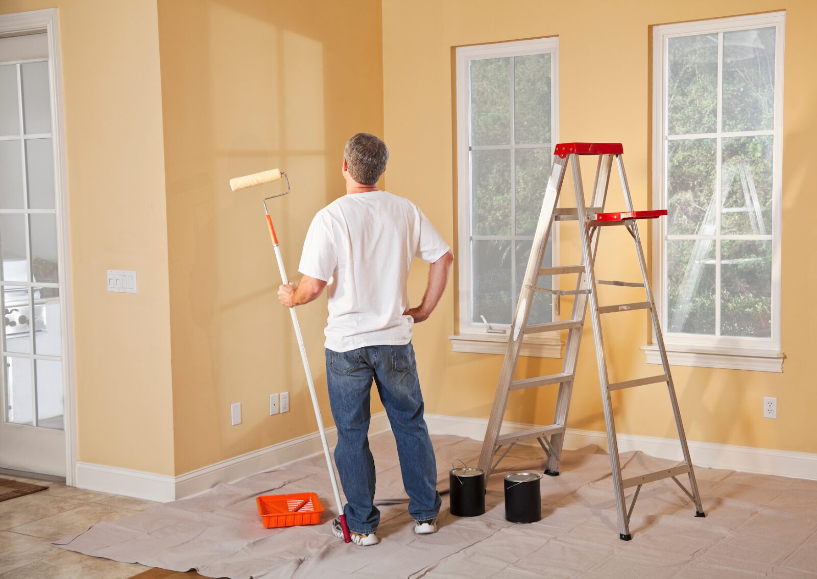 A man is using a roller to paint a yellow interior wall, carefully following a precision painting process.