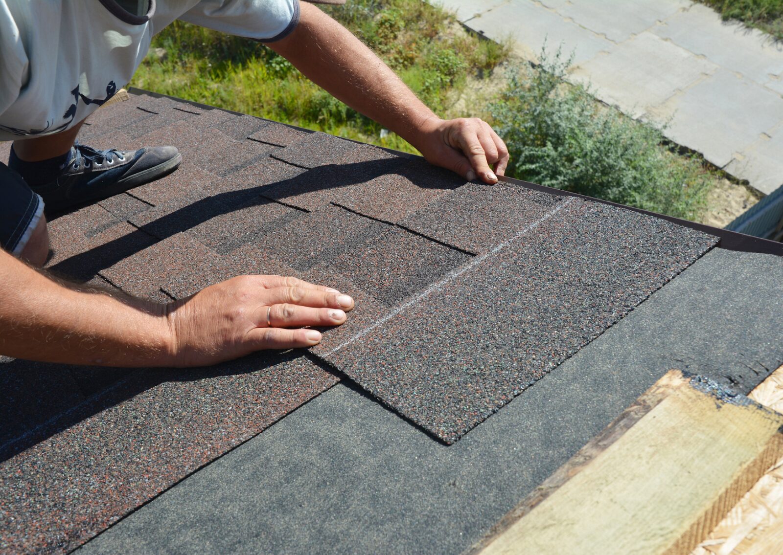 A worker installing asphalt shingles on a roof during a residential roof construction or roof repair project.