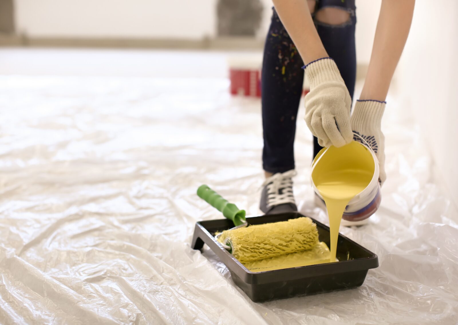 House painting professionals are pouring yellow paint into a tray, preparing tools for interior painting.