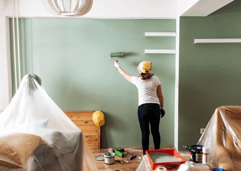 A woman is using a roller to paint a green wall, demonstrating careful preparation and a precise painting process.
