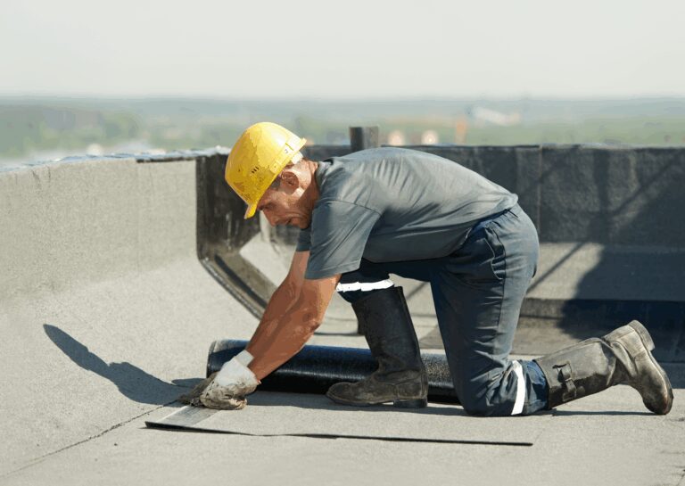 A worker installing material on a flat roof surface for a commercial roofing project, wearing safety gear.