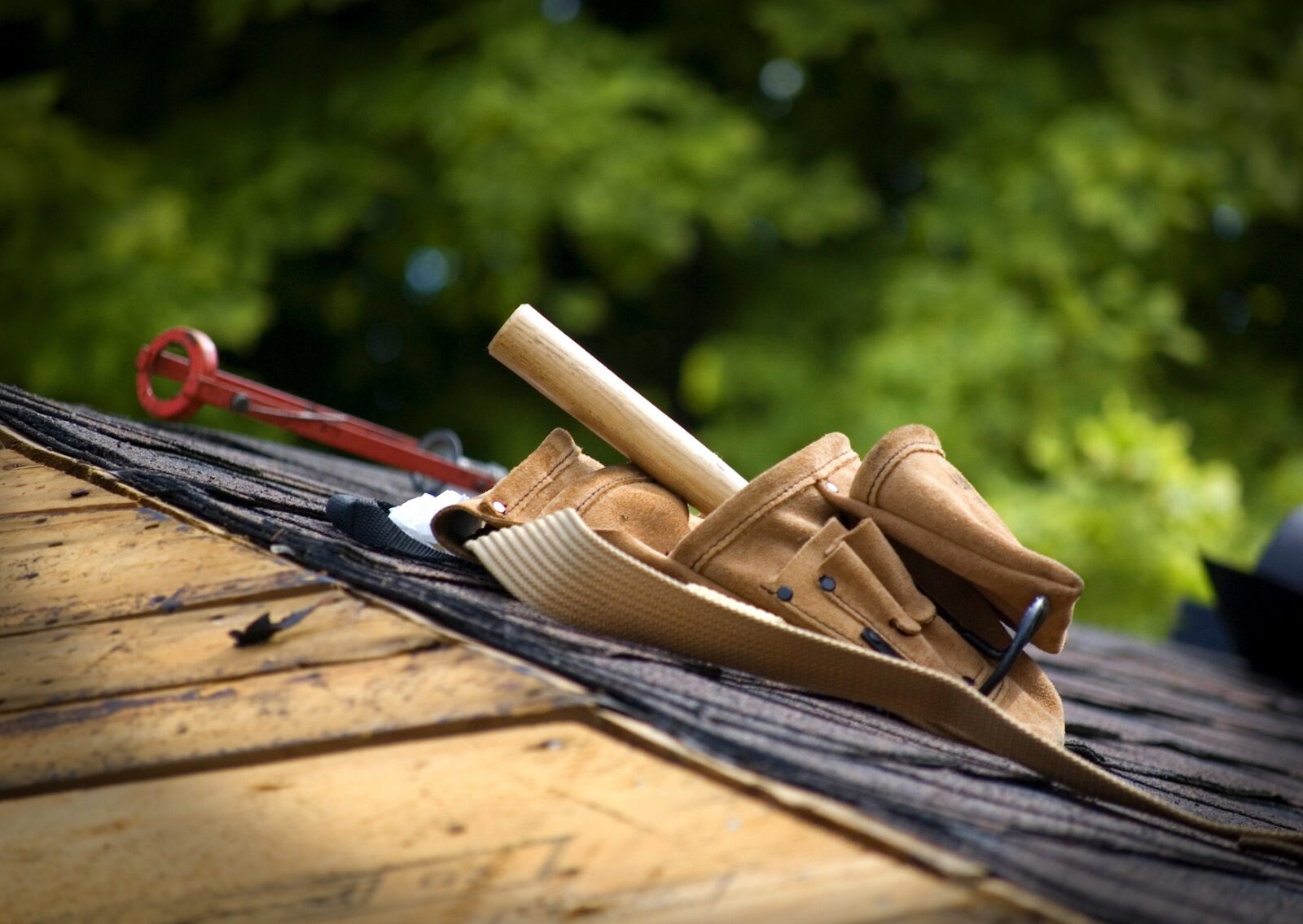 Tool belt and roofing tools resting on partially shingled roof during residential roofing services.