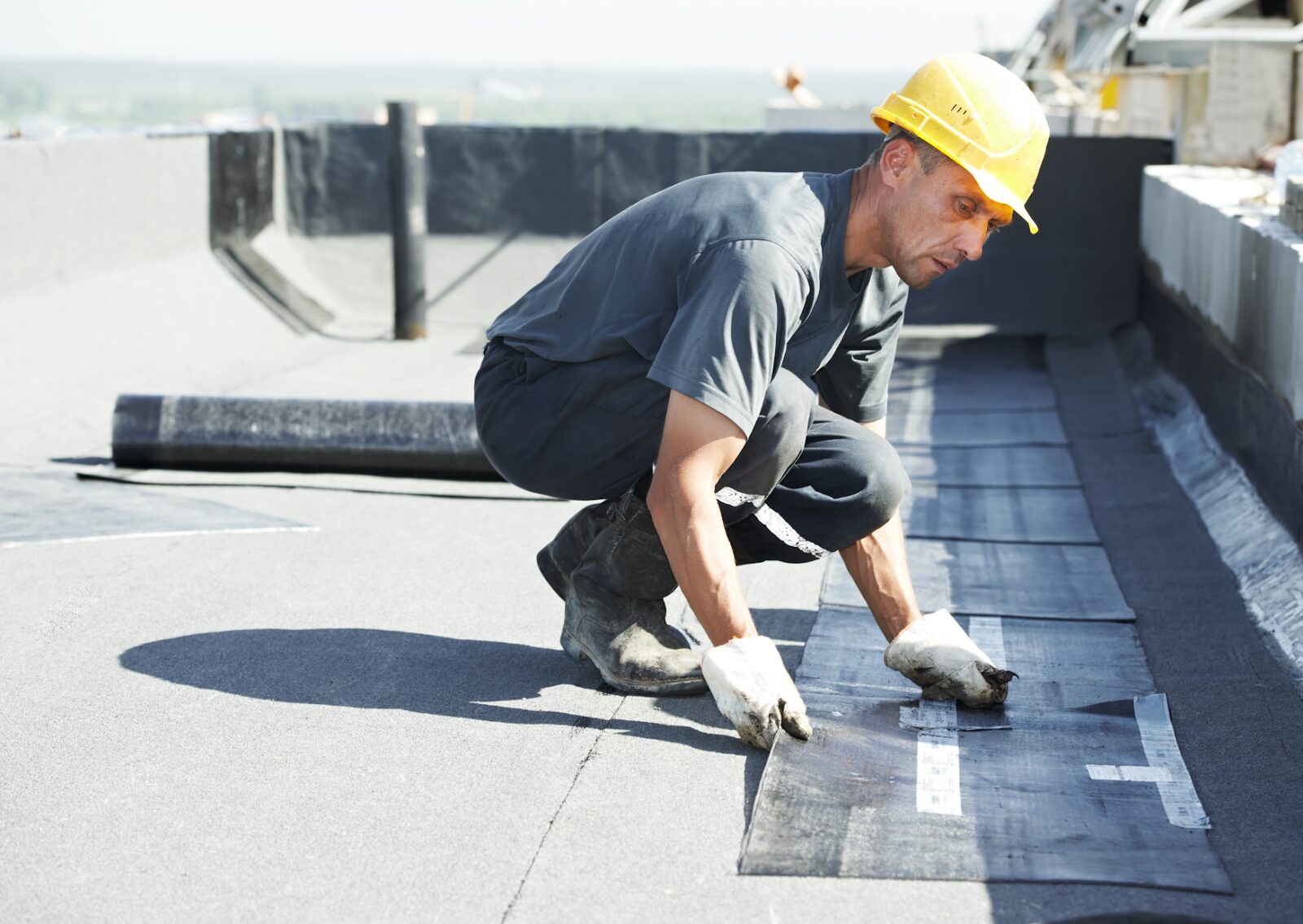 Commercial roofing contractor applying waterproof membrane on a flat roof during a building construction project.